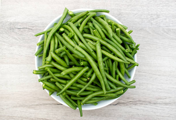 haricots verts crus dans un bol blanc sur une table en bois.  vue d’en haut - green bean photos et images de collection