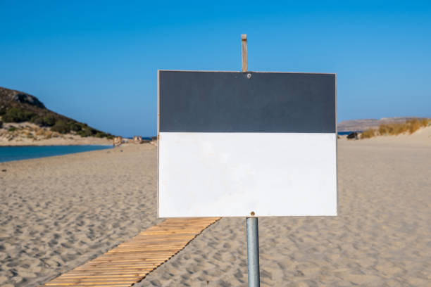 istock Sign white blank board on post blur sandy beach background. Advertise template, copy space. 1353345783