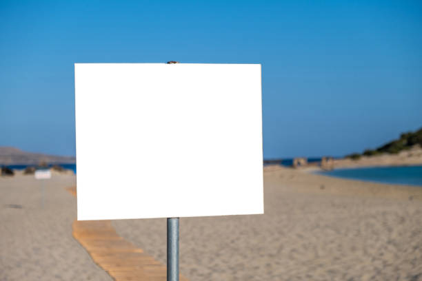 istock Sign white blank board on post blur sandy beach background. Advertise template, copy space. 1353345793
