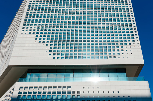 Low angle view on corporate building facade with uneven windows in rows, diminishing perspective towards the clear sky, abstract background