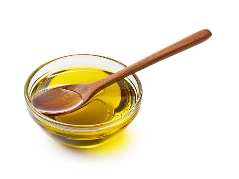Olive oil in a glass bowl and wooden spoon on a white background