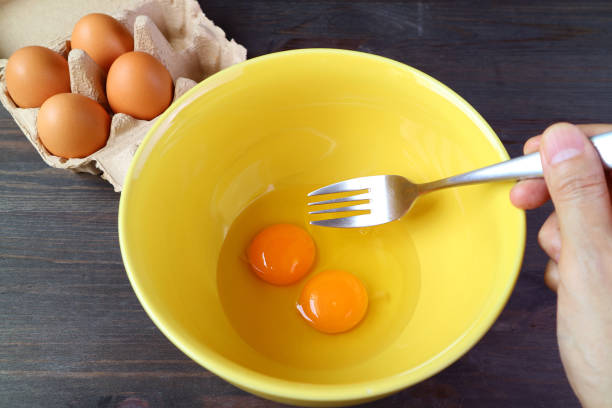 istock Hand holding Fork Going to Beat a Pair of Raw Eggs in a Mixing Bowl 1353350166