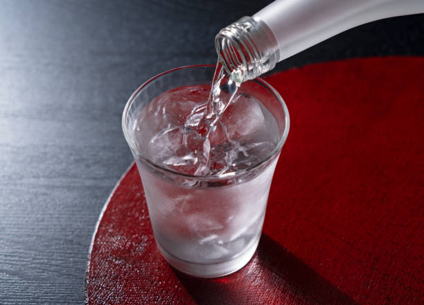 Shochu placed on a red tray against a black background. Shochu on a red tray against a black background. The moment of pouring in a bottle. saki photos stock pictures, royalty-free photos & images