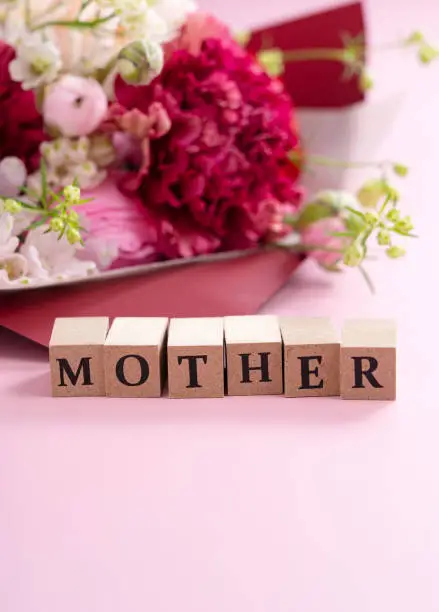 Photo of A bouquet of flowers and a block of text for mother placed on a pink background. Mother's Day image.