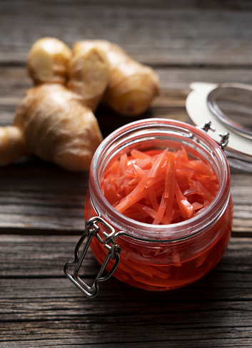 Red pickled ginger in a glass jar set against an old wooden background.