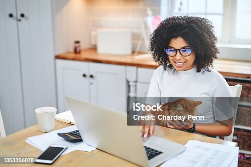 istock Shot of a young woman affectionately holding her cat and using a laptop while working from home 1353356078