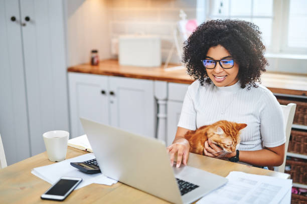 zdjęcie młodej kobiety czule trzymającej kota i korzystającej z laptopa podczas pracy w domu - student loans zdjęcia i obrazy z banku zdjęć