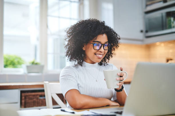 scatto di una giovane donna che usa un laptop e che sta caffè mentre lavora da - corso di formazione foto e immagini stock