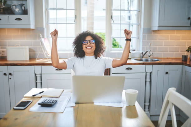 scatto di una bella giovane donna che sembra felice mentre lavora sul suo laptop a casa - paying taxes foto e immagini stock