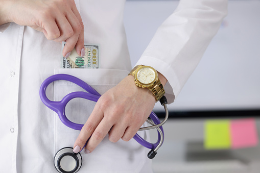 Close-up of woman doctor carry stethoscope tool and show piece of banknote in pocket. Pay to get qualified advice. Corruption in medicine, health concept
