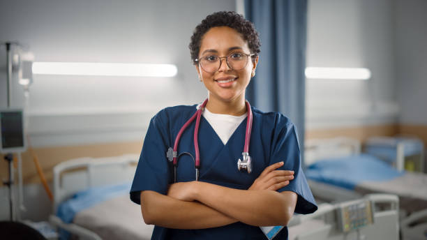 reparto ospedaliero: ritratto di bella infermiera nera in posa, medico, chirurgo sorride in modo affascinante e gentile guarda la fotocamera. clinica moderna con attrezzature avanzate e personale professionale - nurse doctor healthcare and medicine african descent foto e immagini stock