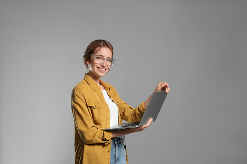 Portrait of young woman with modern laptop on grey background