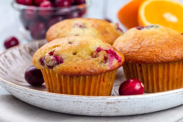 Photo of Homemade cranberry orange muffins on wooden plate, horizontal, closeup