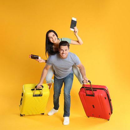 Happy couple with suitcases and passports for summer trip on yellow background. Vacation travel