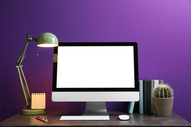 istock Comfortable workplace with modern computer and cactus on table near purple wall. Space for design 1353362801