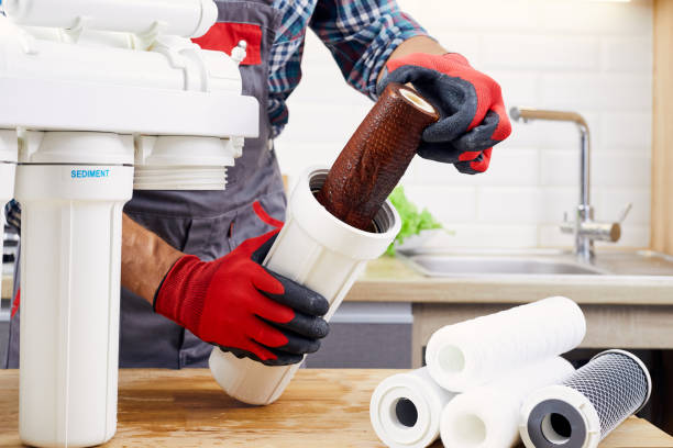 istock Plumber installs or change water filter. Replacement aqua filter. Repairman installing water filter cartridges in kitchen. Installation of reverse osmosis water purification system. 1353364888