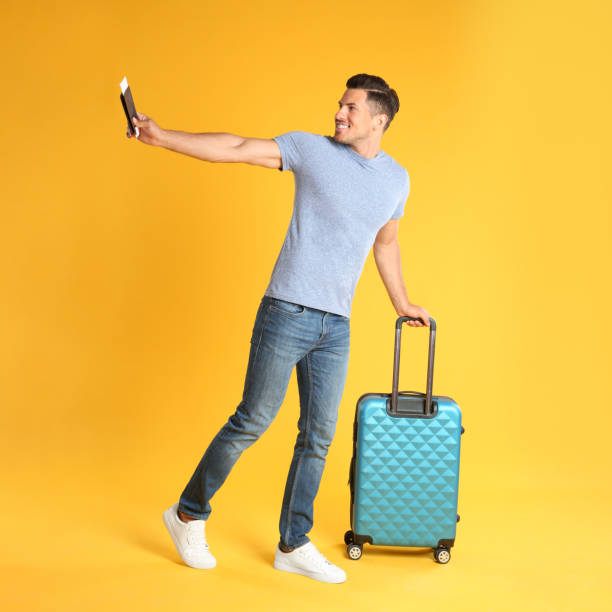 istock Handsome man with suitcase and ticket in passport for summer trip on yellow background. Vacation travel 1353365446