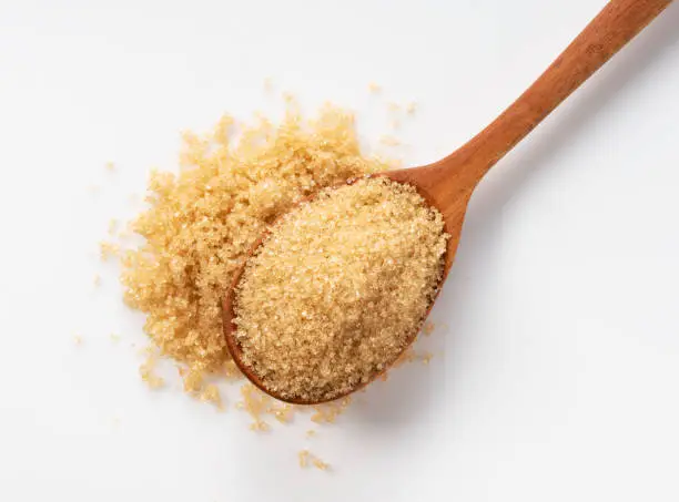 Photo of Wooden spoon and brown sugar on a white background.