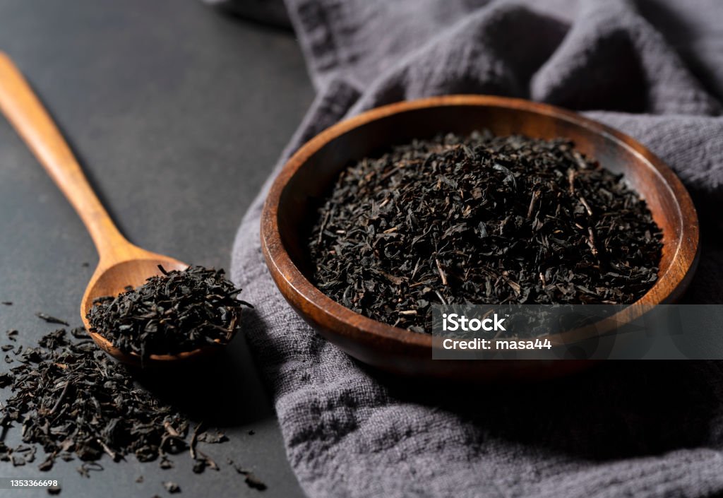 Tea leaves in a wooden plate and spoon on a black background. Tea leaves in a wooden plate and spoon on a black background. Asian style Dried Tea Leaves Stock Photo