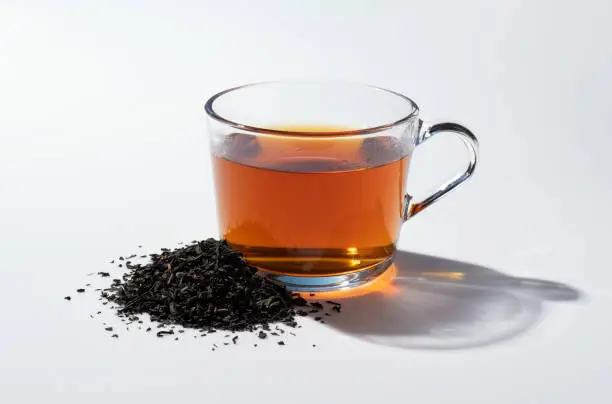 Hot tea and tea leaves in a glass on a white background