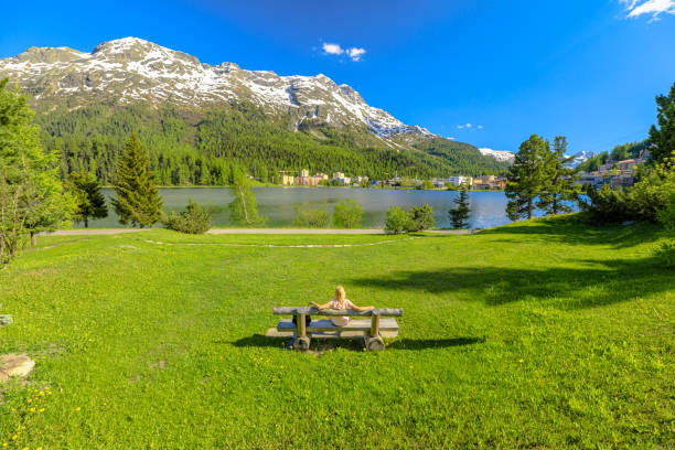 Woman on bench of St. Moritz traveler woman sitting on a park bench of St. Moritz by Lake St. Moritz in Switzerland. St. Moritz lakefront in Grisons Canton in Maloja region. maloja region stock pictures, royalty-free photos & images