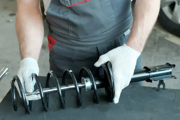 Photo of Car spare parts. Shock absorber strut and spring in the hands of a mechanic, close-up.