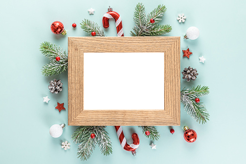 Christmas or Happy New Year photo frame with fir tree branches, holiday decorations on blue background. Flat lay. Mock up. Top view
