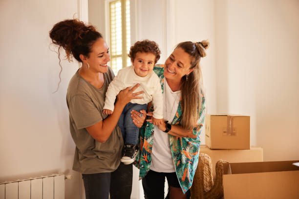 A female LGBT couple with a child moves to a new home. Portrait of a couple moving into a new home with their baby boy. lesbian stock pictures, royalty-free photos & images