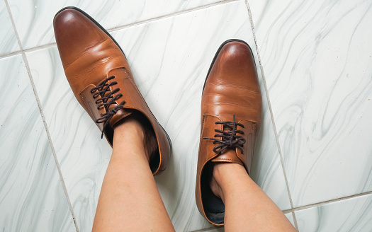 top view  woman feet try to wear oversize brown men leather shoes