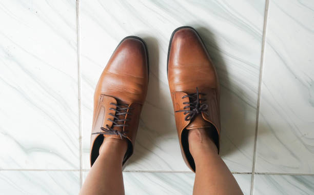 top view of woman feet wearing oversize brown men leather shoes stock photo