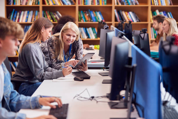 studentin, die an computer in der bibliothek arbeitet und von einem tutor unterstützt wird - postsekundäre bildung stock-fotos und bilder