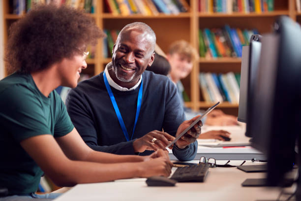 male university or college student working at computer in library being helped by tutor - senior adult african descent men black imagens e fotografias de stock