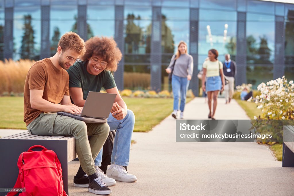 Male University Or College Students Sitting Outdoors On Campus Talking And Working On Laptop Campus Stock Photo