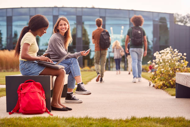 istock Female University Or College Students Sitting Outdoors On Campus Talking And Working On Laptop 1353373014