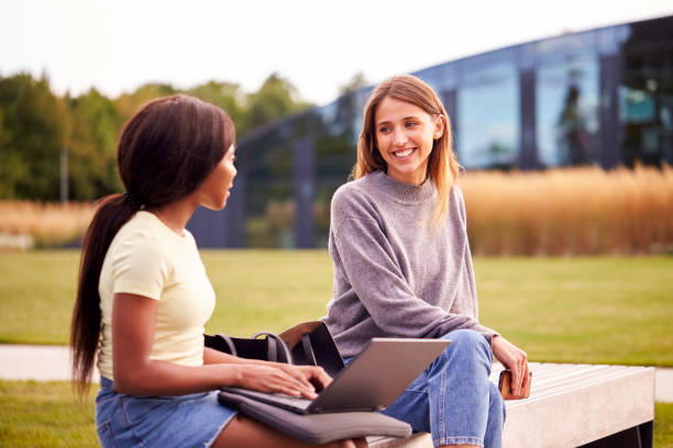 istock Female University Or College Students Sitting Outdoors On Campus Talking And Working On Laptop 1353373242