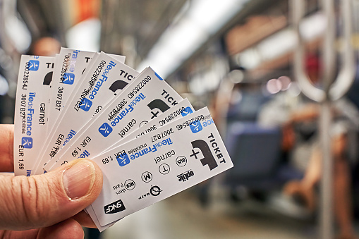Paris, France - September 30, 2021: Fanned out metro tickets in hand in front of defocused subway interior.