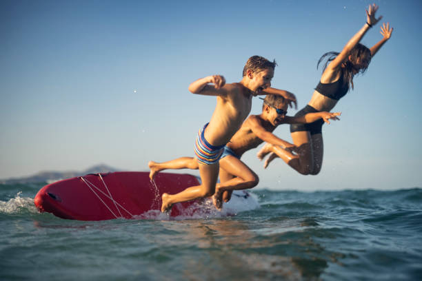 Three kids jumping from the SUP paddleboard into the sea