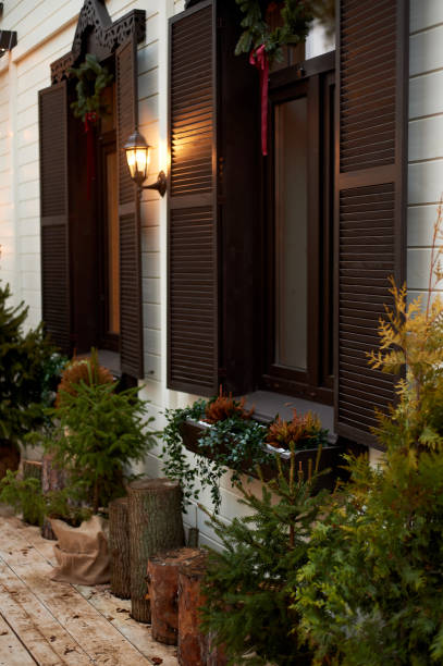 istock Windows with dark wooden shutters and decorative greenery. Cottage 1353375643