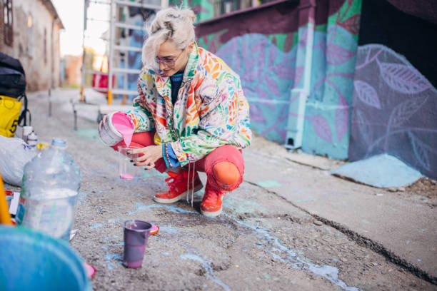 One woman, young female street artist preparing colors for painting on a building wall outdoors.