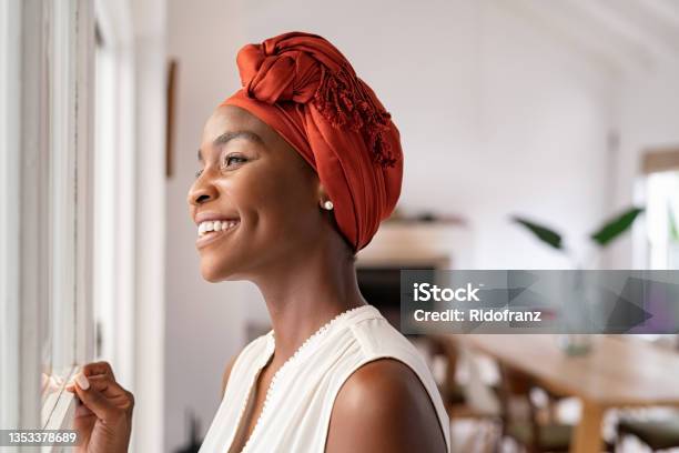 African Woman Looking Out Of Window While Wearing Traditional Turban Stock Photo - Download Image Now