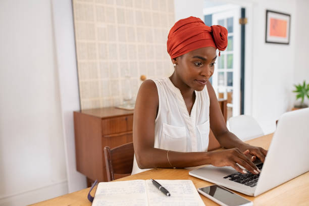 Mature african american woman working on laptop from home Mature black woman with traditional turban sitting at home while working on laptop. Successful black businesswoman typing on laptop wearing a traditional turban while working from home with copy space. Mid adult entrepreneur using computer during lockdown. turban stock pictures, royalty-free photos & images