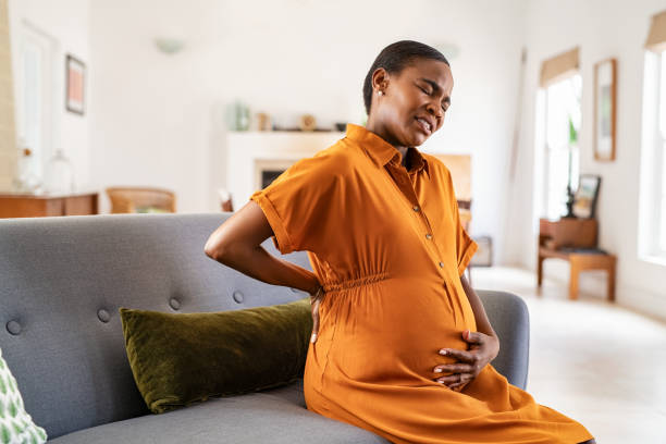 Pregnant african american woman having backache during gestation Mature pregnant woman having a backache while relaxing on couch at home. Unhappy black expecting woman suffering from lower back pain sitting on sofa with copy space. Tired middle aged african pregnant woman suffer from lower back pain on last month of pregnancy. uncomfortable stock pictures, royalty-free photos & images