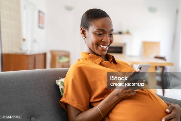 Smiling Pregnant Mid Adult Black Woman Messaging On Mobile Phone Stock Photo - Download Image Now