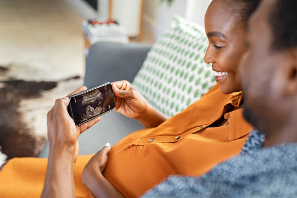 schwangeres schwarzes paar, das ultraschall am telefon beobachtet - human pregnancy telephone ultrasound family stock-fotos und bilder