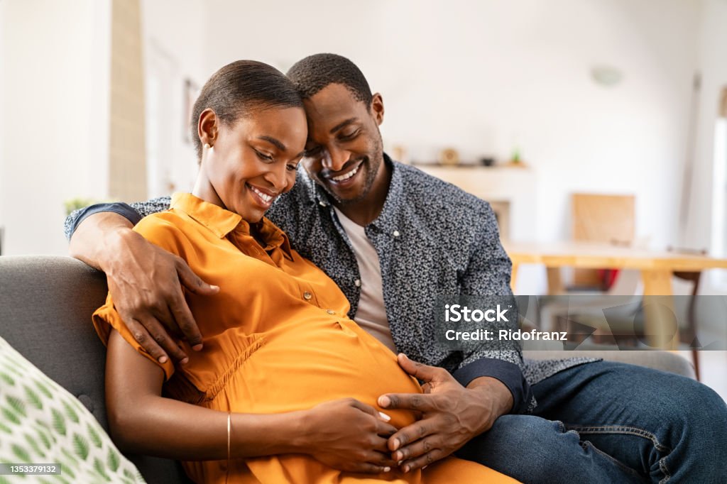 Black expectant parents sitting on sofa dreaming about their baby - 免版稅懷孕圖庫照片