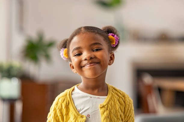 Cute little african american girl looking at camera Smiling cute little african american girl with two pony tails looking at camera. Portrait of happy female child at home. Smiling face a of black 4 year old girl looking at camera with afro puff hair. messing about stock pictures, royalty-free photos & images