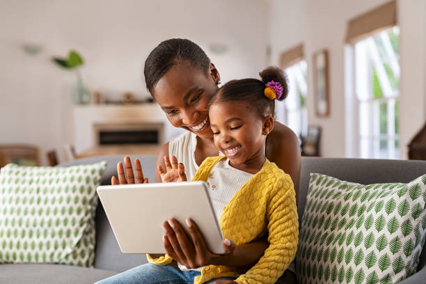 mignonne petite fille et mère africaine utilisant une tablette numérique pour passer un appel vidéo - sofa family fun child photos et images de collection