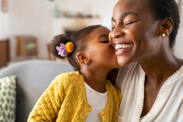 Cute little girl kissing mother on cheek Close up of beautiful daughter kissing mother on cheek at home. African american little girl giving kiss to happy mother. Lovely black female child kissing cheerful and proud woman on cheek with copy space for mother's day. mothers day stock pictures, royalty-free photos & images