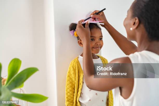 Mother Measuring Daughters Height And Marking On Wall At Home Stock Photo - Download Image Now