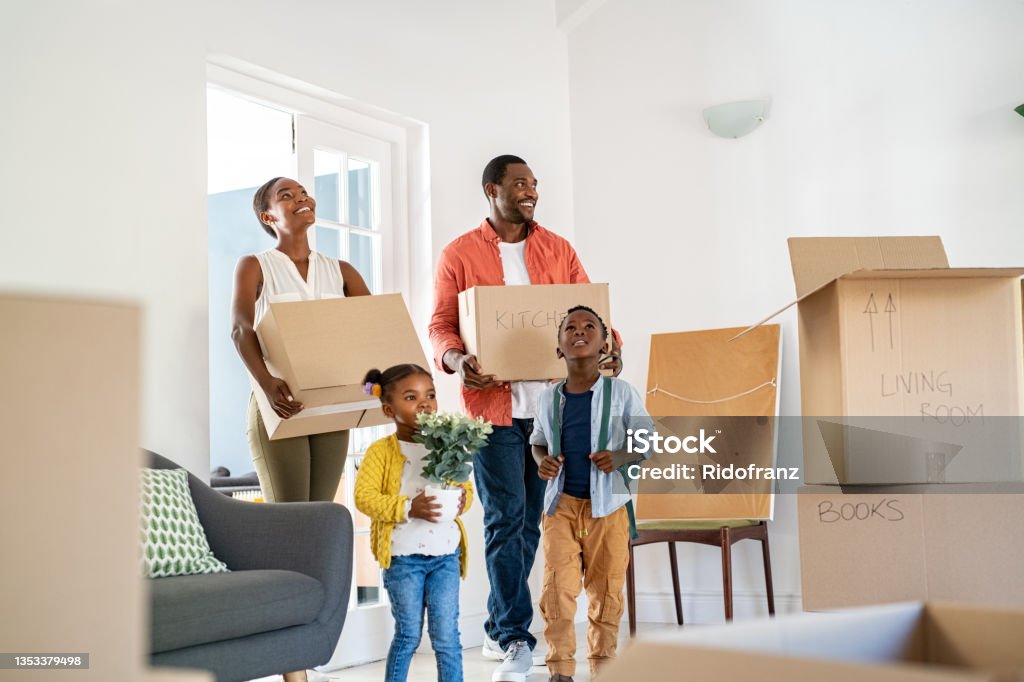 Black family with two children moving house Beautiful african american family with two children carrying boxes in a new home. Cheerful mature mother and mid adult father holding boxes while entering new home with son and daughter. Happy son and daughter helping parents relocating in new house with copy space. Moving House Stock Photo